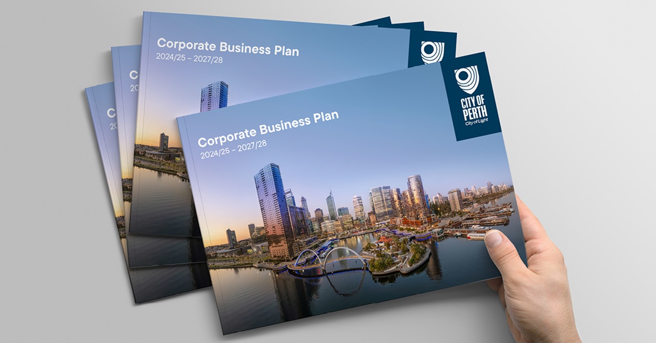 Person taking a copy of the 2024 2025 Corporate Business Plan from a pile of documents