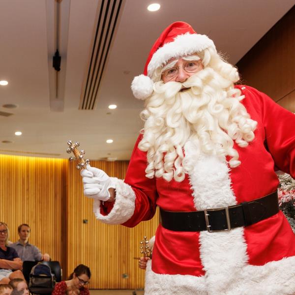 Photo of Santa in the Library auditorium with a crowd of parents and a Christmas tree in the background.