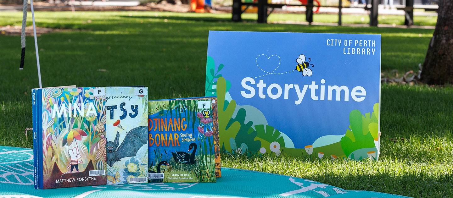 Storytime sign and library books on a picnic rug at the park.
