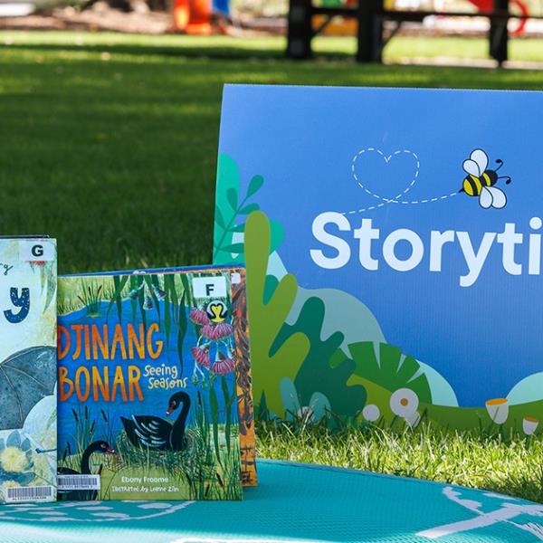 Storytime sign and library books on a picnic rug at the park.