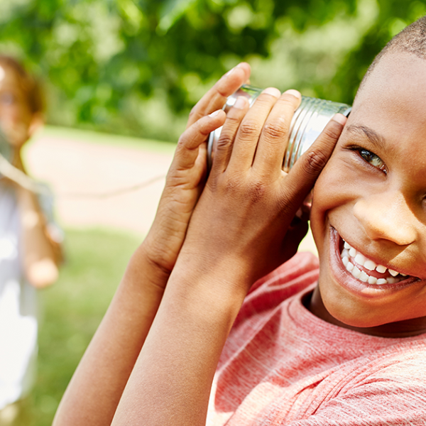 Two children playing with a tin-can telephone outside in a park.