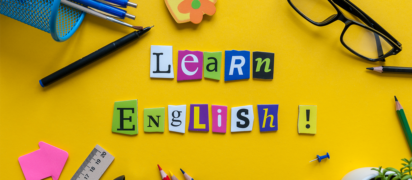 Cut out lettering saying Learn English, surrounded by stationery and on a yellow background.