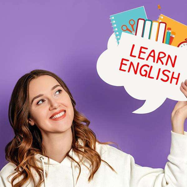 Young female student in cream hoody holding up a learn English speech bubble