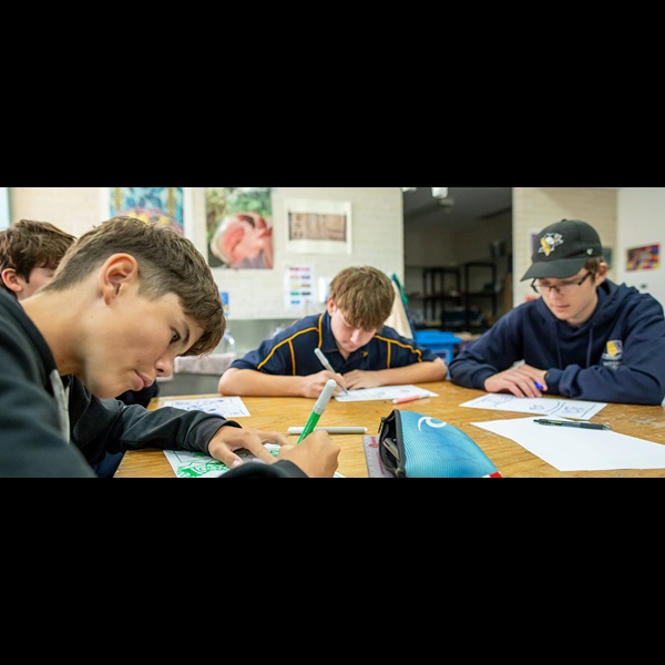Students in uniform sat around a table, producing artwork.