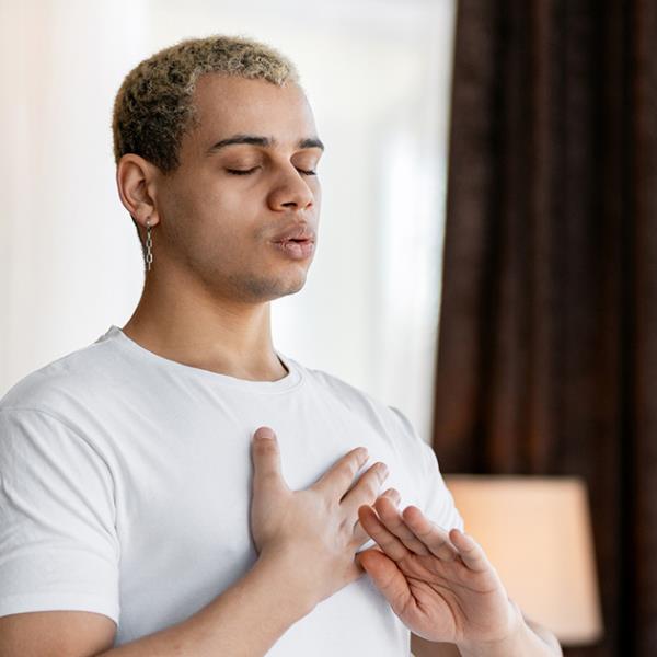 Young man with eyes shut and hands on chest doing breathing exercises.