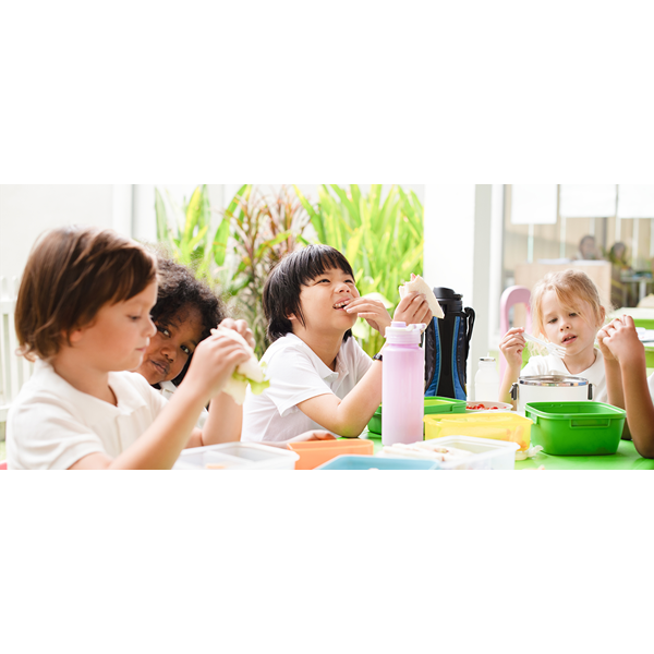 A group of children sat around a table eating a healthy packed lunch.