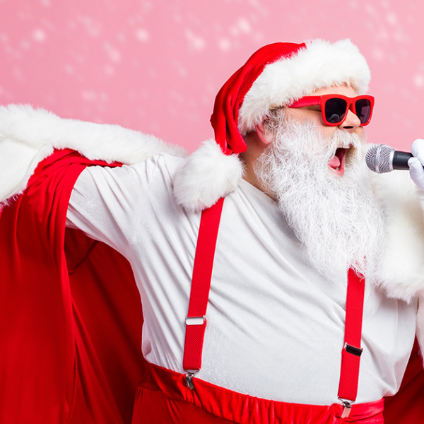 Man dressed as Santa singing a rocking song into a handheld microphone.