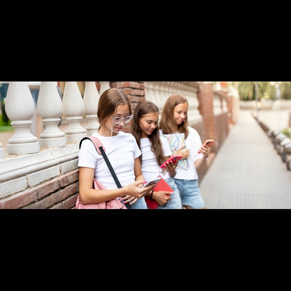Three teenage girls leaning against a brick wall looking at their phones