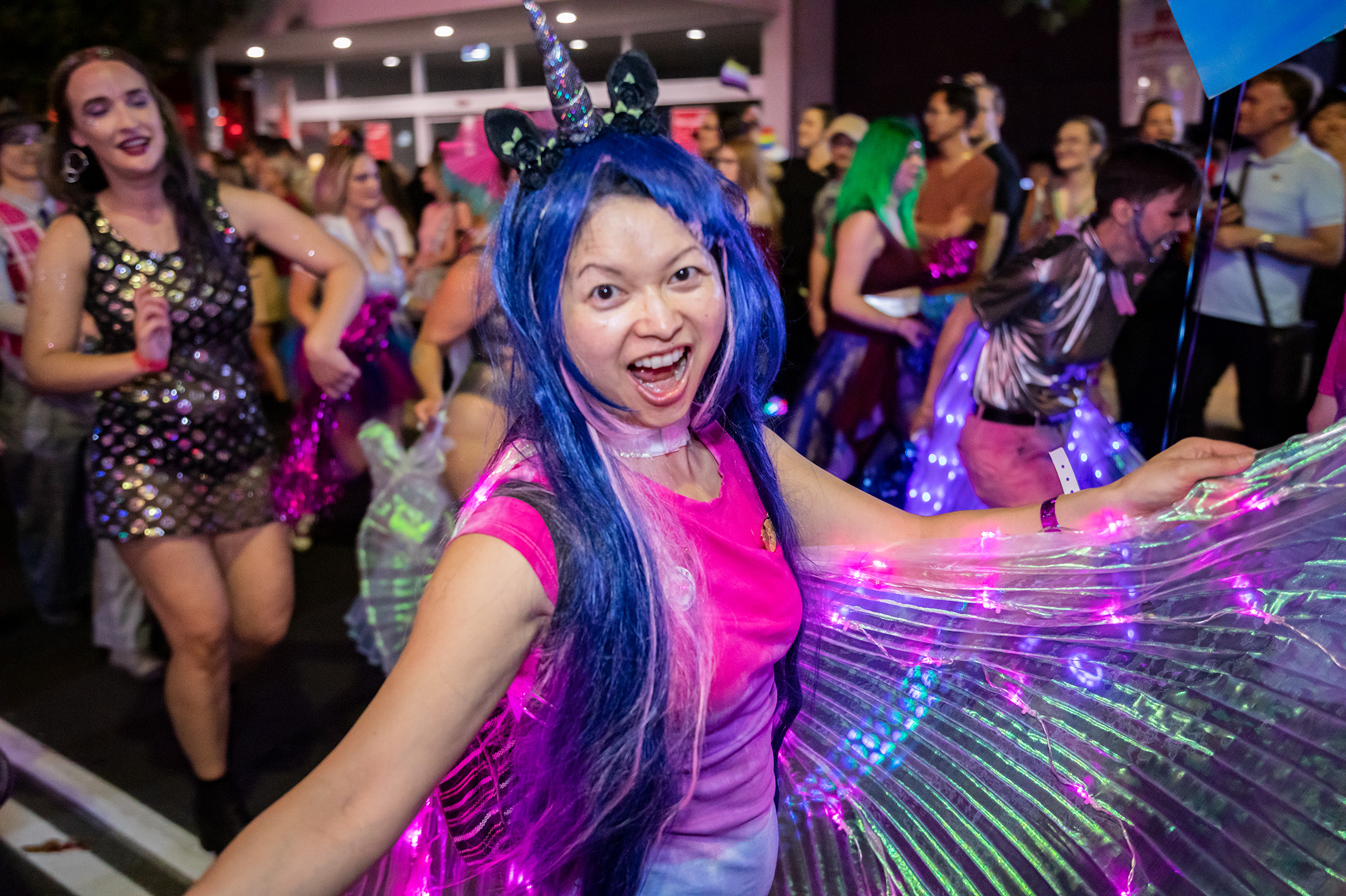 Pride parade participant in long blue wig with unicorn horn and wings