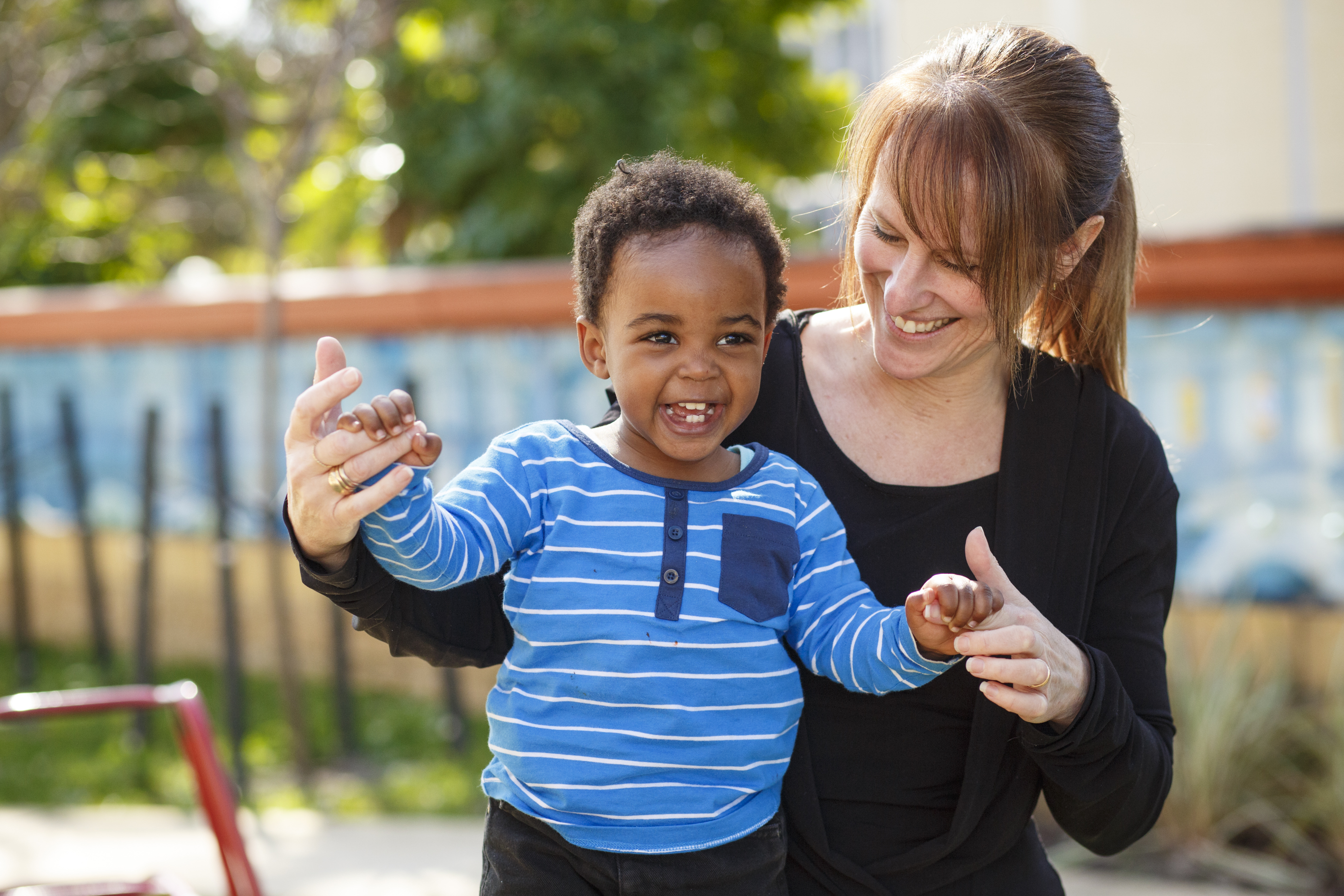 Childcare worker holding the hands of a smiling child.