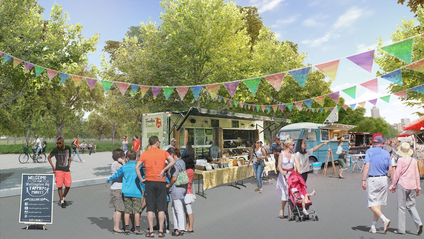 People gathering at a busy market with trees, stalls and bunting.