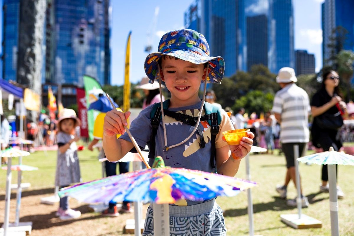 Young girl doing a painting activity at a City event with a fair in the background