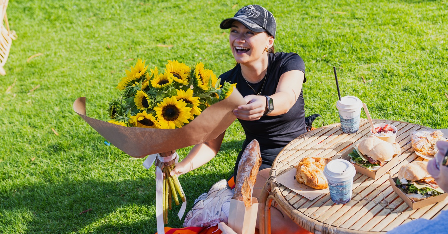 A happy market visitor with a bright bunch of sunflowers and a table full of food