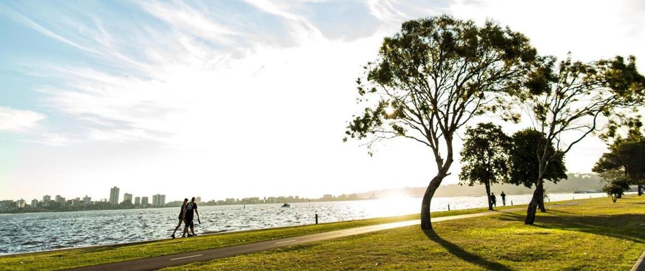 Swan River Foreshore with walkers along the footpath and the sun shining, and some green trees