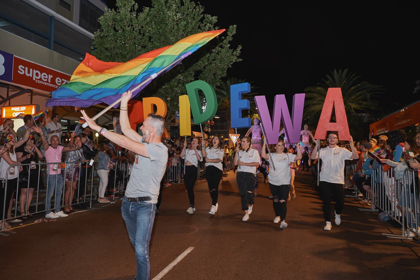Man holding rainbow flag in parade in front of PRIDE WA letters